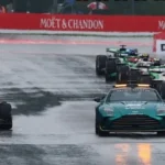 Monoplazas de Fórmula 1 detenidos detrás del safety car durante una carrera bajo condiciones de pista mojada.