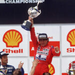 Ayrton Senna celebra exhausto en el podio del Gran Premio de Brasil 1991 en Interlagos, sosteniendo el trofeo y haciendo delirar a todo Brasil.