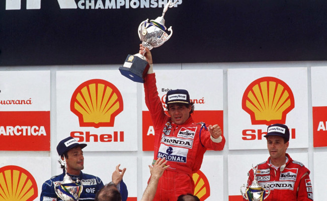 Ayrton Senna celebra exhausto en el podio del Gran Premio de Brasil 1991 en Interlagos, sosteniendo el trofeo y haciendo delirar a todo Brasil.